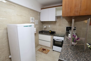 A compact kitchen with a refrigerator, stove, oven, and a small sink. - Incrível suíte em Manaíra por Carpediem (João Pessoa)