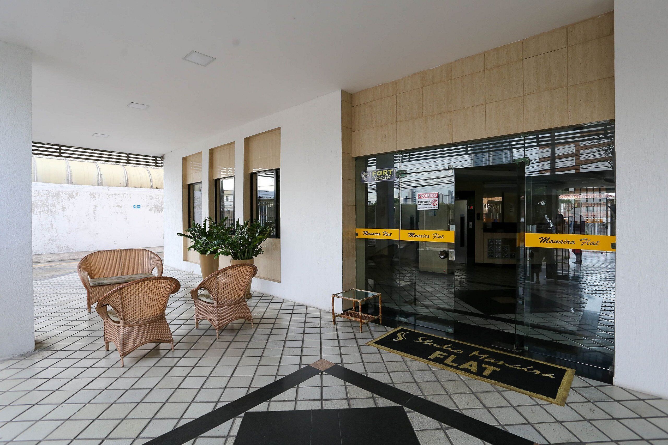 Un vestíbulo de hotel con sillas de mimbre, una planta en maceta y un suelo de baldosas.