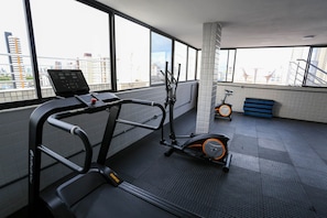 Ein Fitnessraum mit Laufband, Crosstrainer und Ergometer, großen Fenstern mit Stadtblick und einem gefliesten Boden.