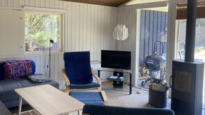 A cozy living room with a wooden ceiling, a sofa, a blue chair, a small table, a TV, and a wood-burning stove. - Cozy cottage 250 m. from the beach. (Nykøbing sj.)