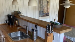 A kitchen with wooden countertops, a sink, hanging utensils, and a painting on the wall. - Cozy cottage 250 m. from the beach. (Nykøbing sj.)