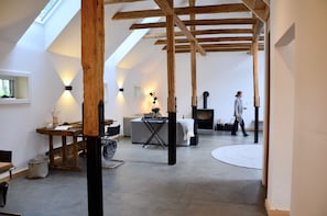 A spacious loft with exposed wooden beams, a fireplace, and a large window.