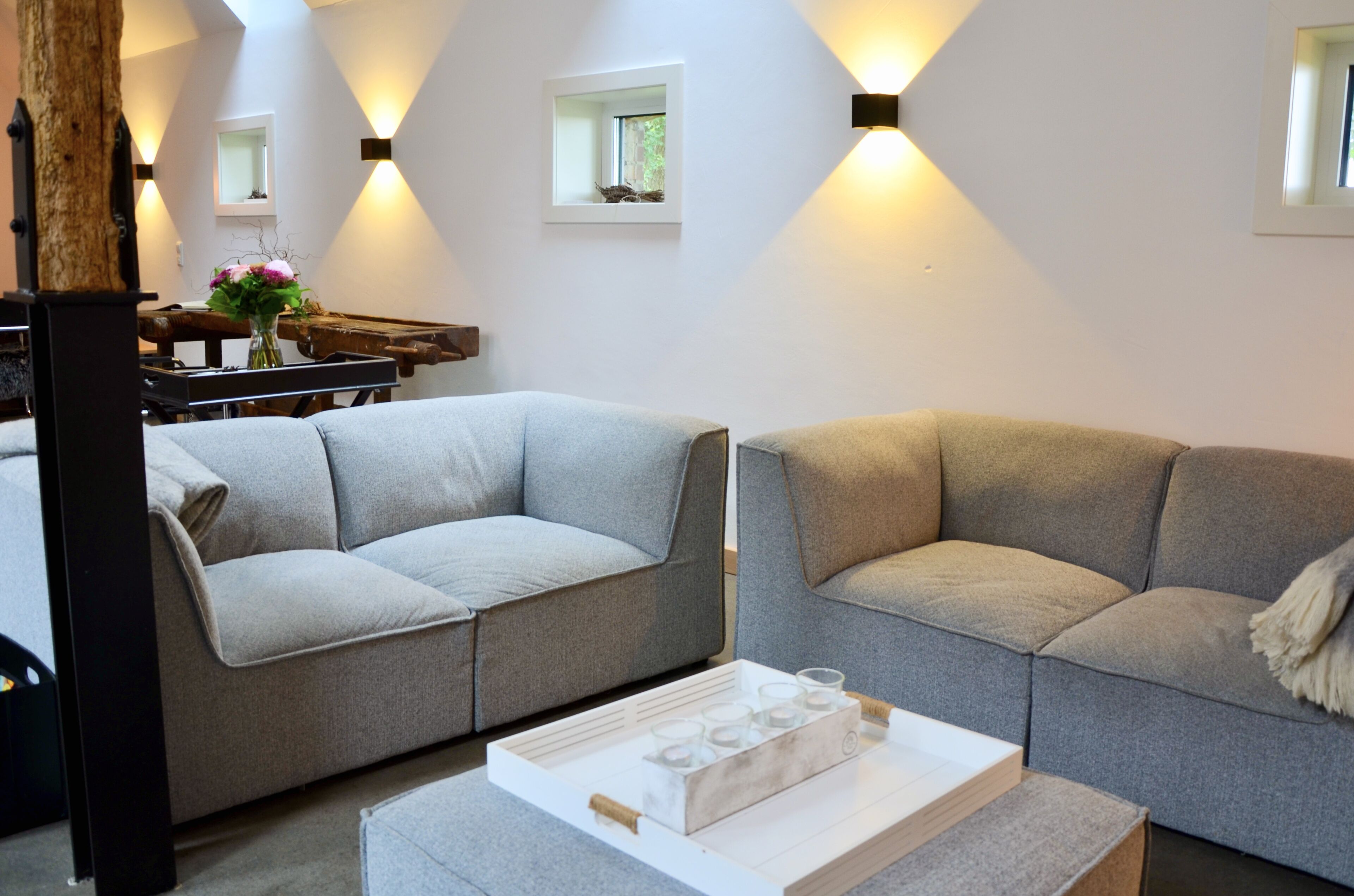 A modern living room with two grey sofas, a wooden coffee table with candles, and wall-mounted lights.