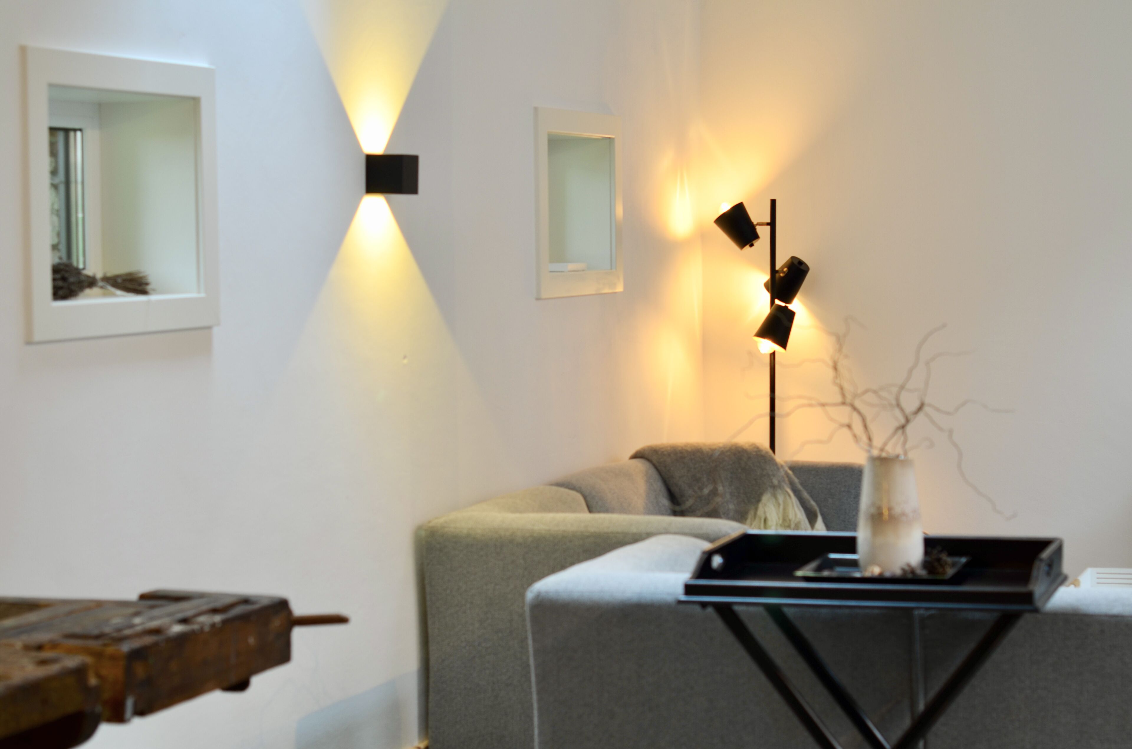 Uma sala de estar moderna com um sofá, uma mesa de centro e duas luminárias fixadas na parede.