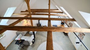 Une pièce de style loft avec des poutres apparentes, un canapé, une petite table agrémentée d’un vase de fleurs et une cheminée.