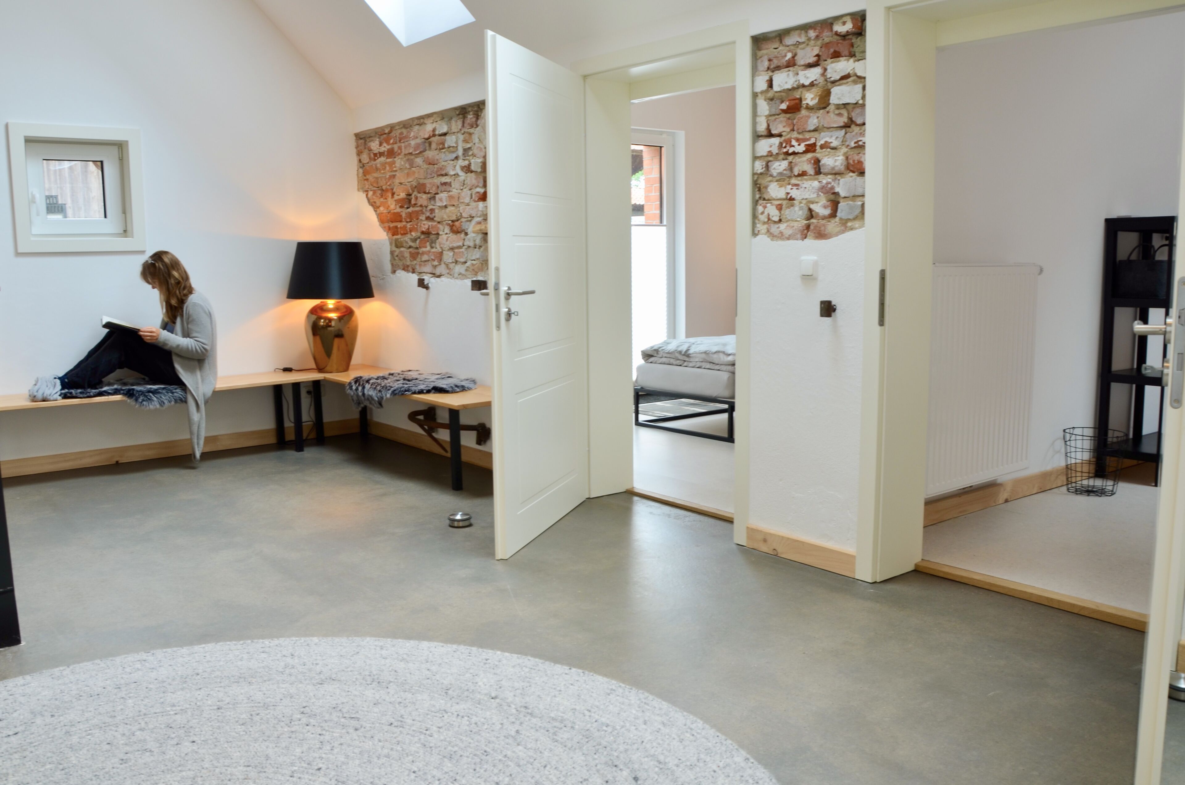 A modern, well-lit room with a skylight, a reading area with a bench, a lamp, and a bed with a white headboard.