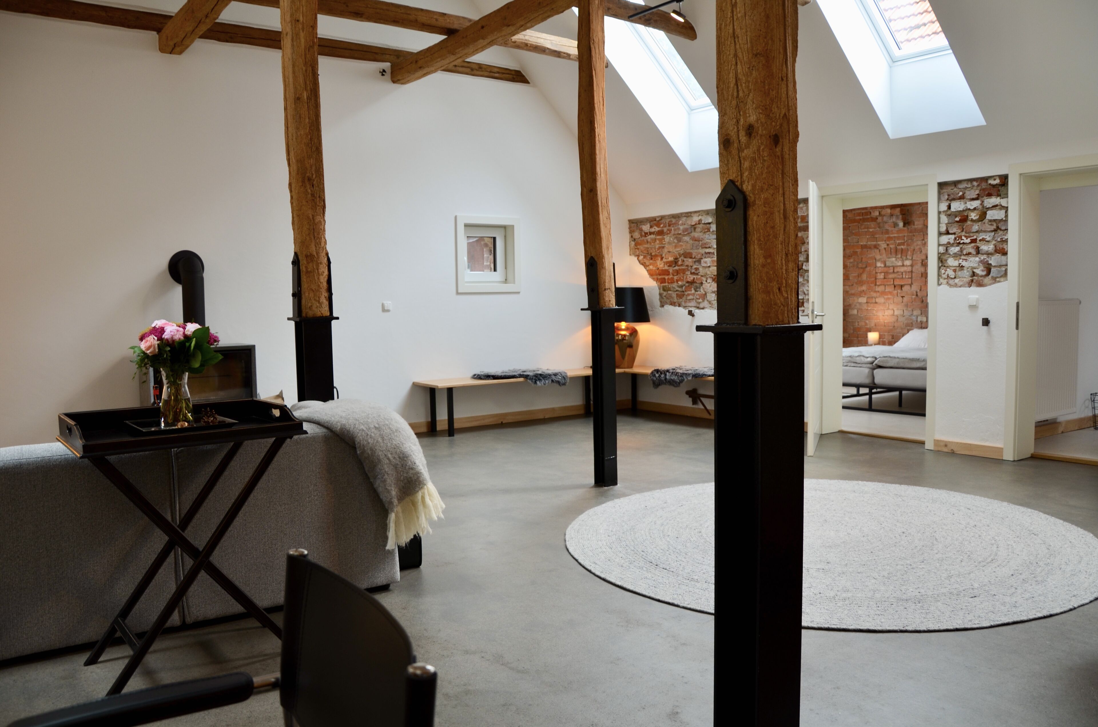 Une chambre spacieuse aménagée en mezzanine, avec des poutres apparentes, une lucarne, une cheminée chaleureuse et un mur en briques rustiques.