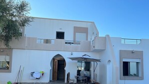 A two-story building with a patio area featuring a table and chairs, a pool, and a grassy lawn. - Villa (Gouvernement Medenine)