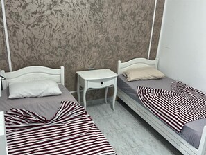 Ein kleines, ordentliches Schlafzimmer mit zwei Einzelbetten, einem kleinen Nachttisch und einer gemusterten Decke.
