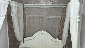 A bed with a white headboard and a grey bedspread, surrounded by white curtains and a decorative canopy. - Villa (Gouvernement Medenine)