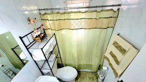 Een kleine badkamer met toilet, een plank met handdoeken en een douchegordijn.