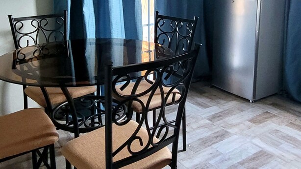 Een eetgedeelte met een tafel, stoelen, een koelkast en gordijnen.
