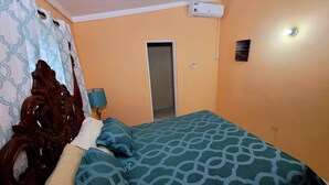 Een slaapkamer met een houten hoofdbord, een bed met een decoratieve spreideken, een bedlampje en een airconditioner aan de muur.