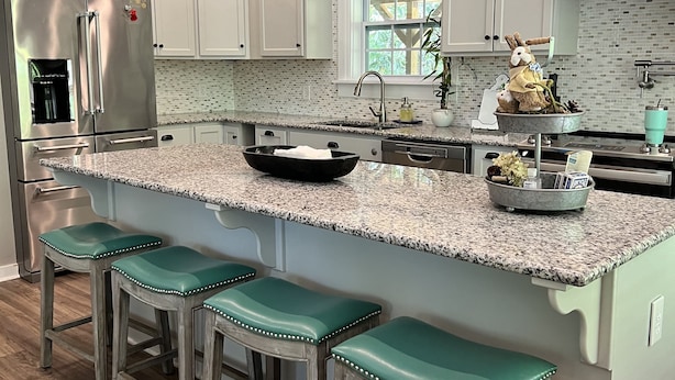 Una cocina moderna con gabinetes blancos, encimera de granito y refrigerador de acero inoxidable.