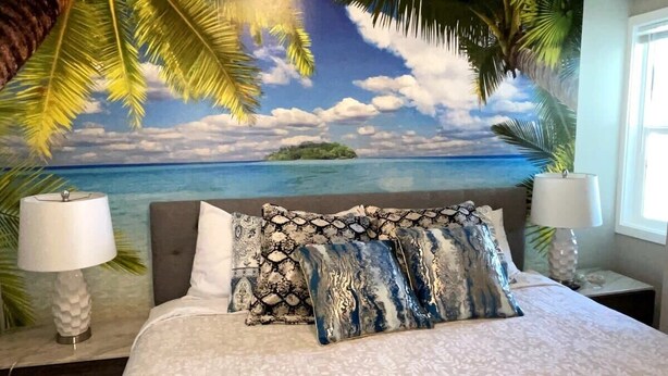 Un dormitorio con cama, almohadas, una mesita de noche y una lámpara.