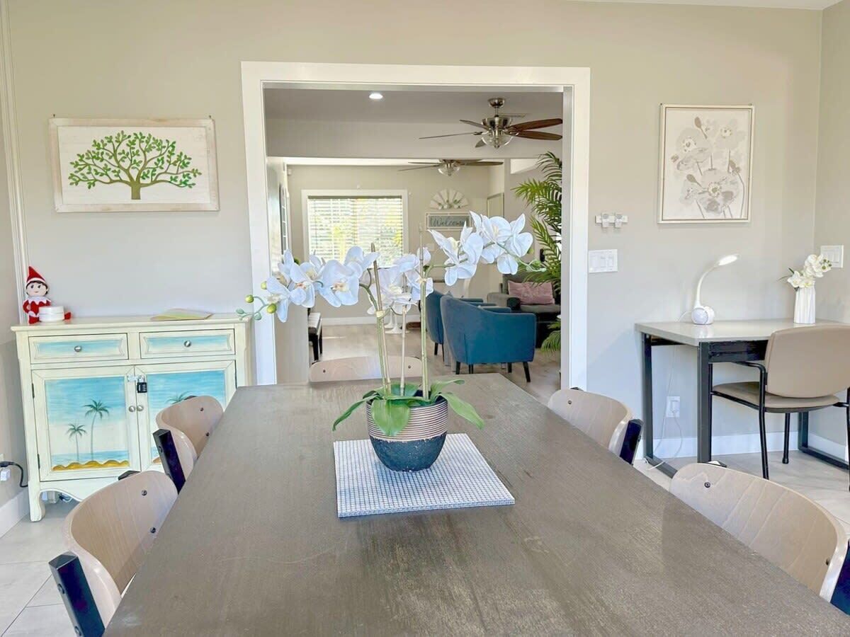 A dining area with a long table, chairs, a potted plant, and a cabinet with a tropical design.