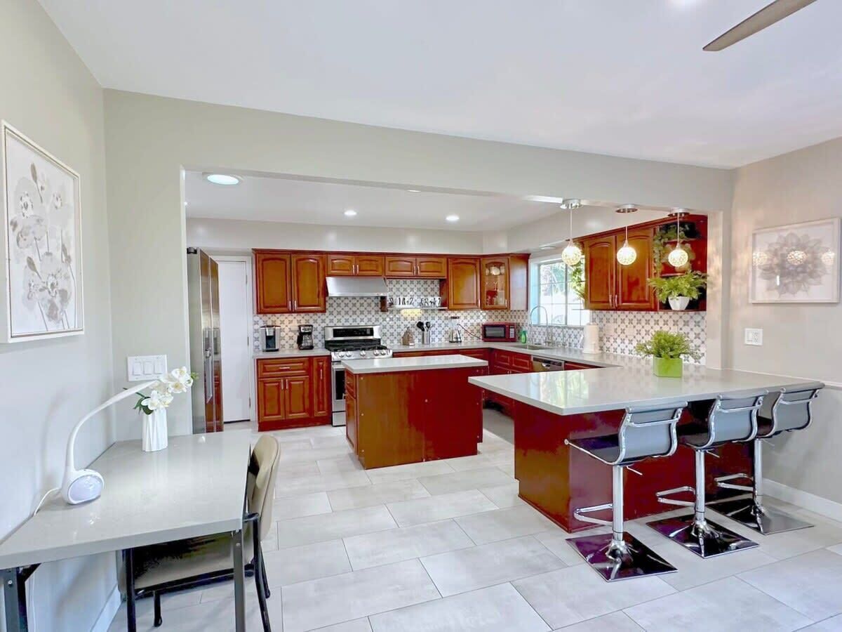 A modern kitchen with wooden cabinets, a central island with bar stools, and a dining area with a table and chairs.