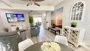 Una sala moderna con un sofá gris, una mesa de comedor con un florero, un televisor montado en la pared y un aparador decorativo.