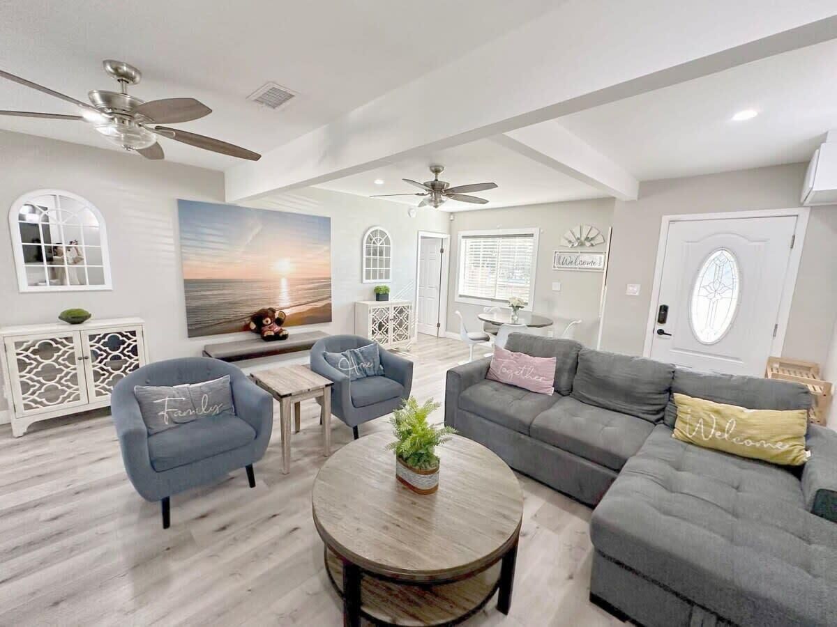 A spacious living room with a gray sofa, two armchairs, a coffee table, and a ceiling fan.