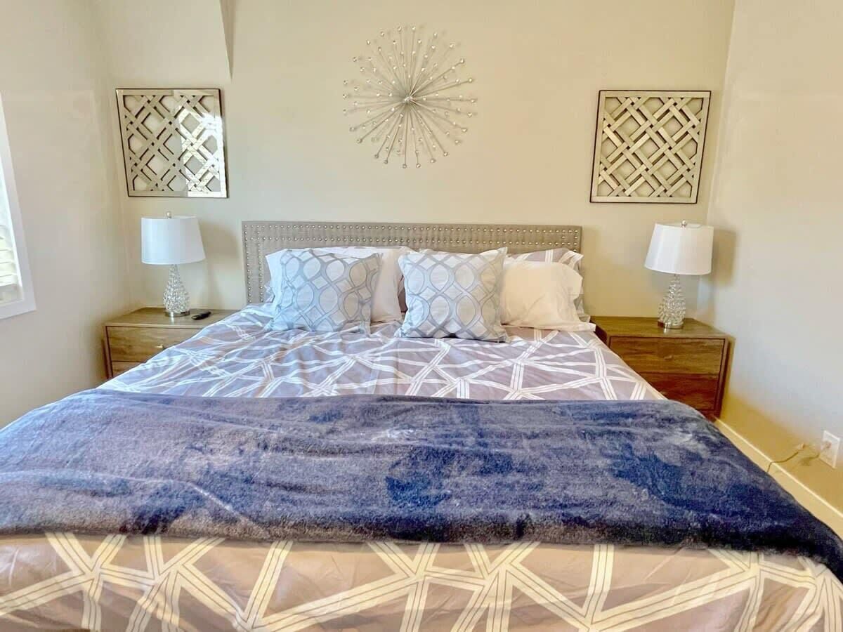 A bed with a patterned bedspread, two bedside tables with lamps, and decorative wall art.