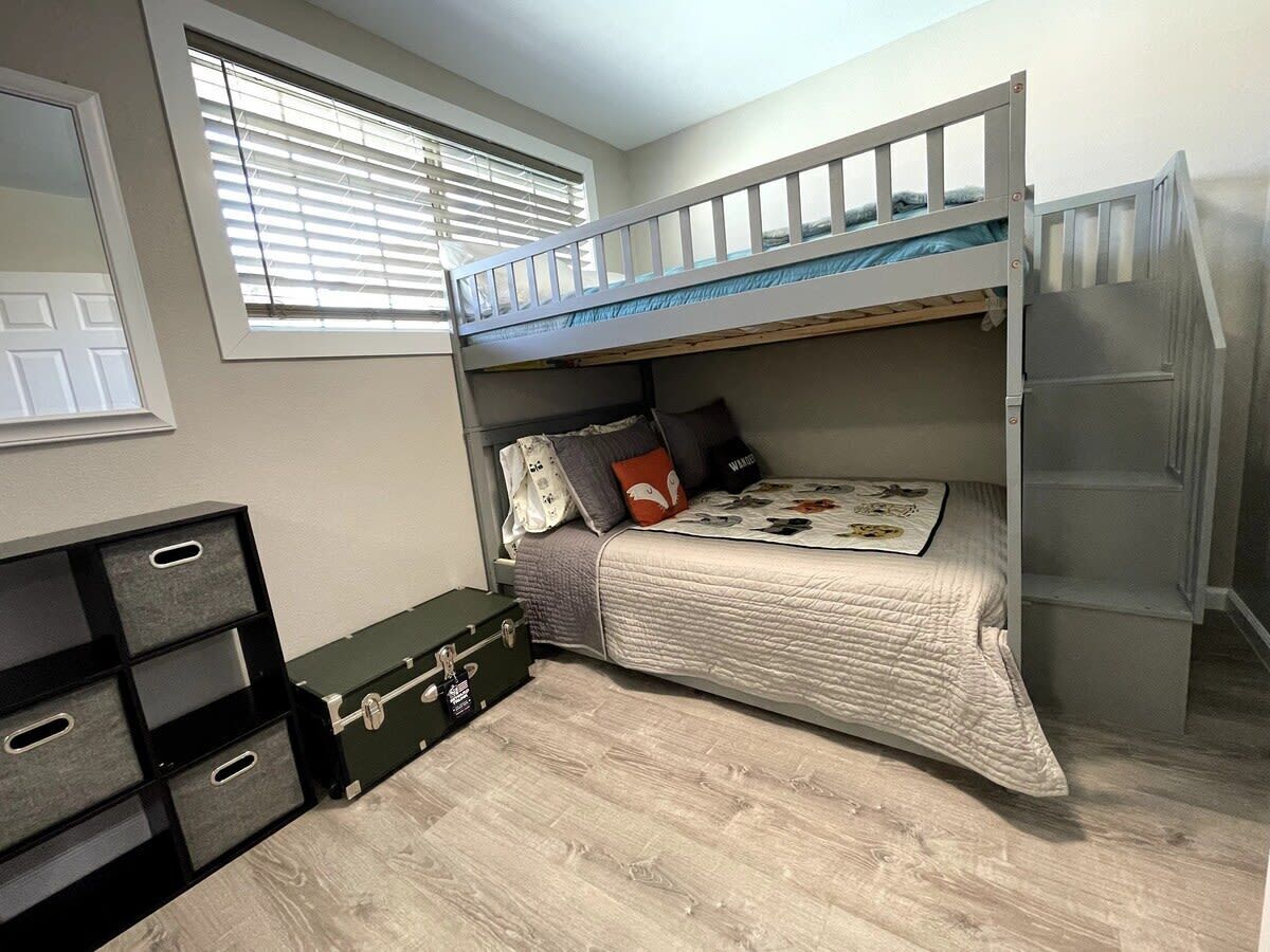 A bunk bed room with a window, storage unit, and a suitcase.