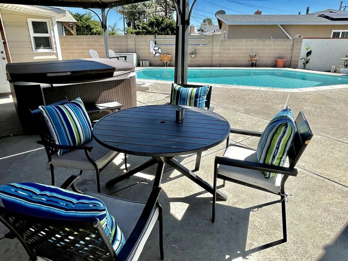 Un patio al aire libre con una mesa redonda y cuatro sillas, una parrilla para barbacoa y una piscina al fondo.