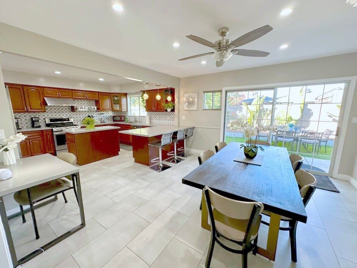 A modern kitchen with a central island, bar stools, and a dining table with chairs.
