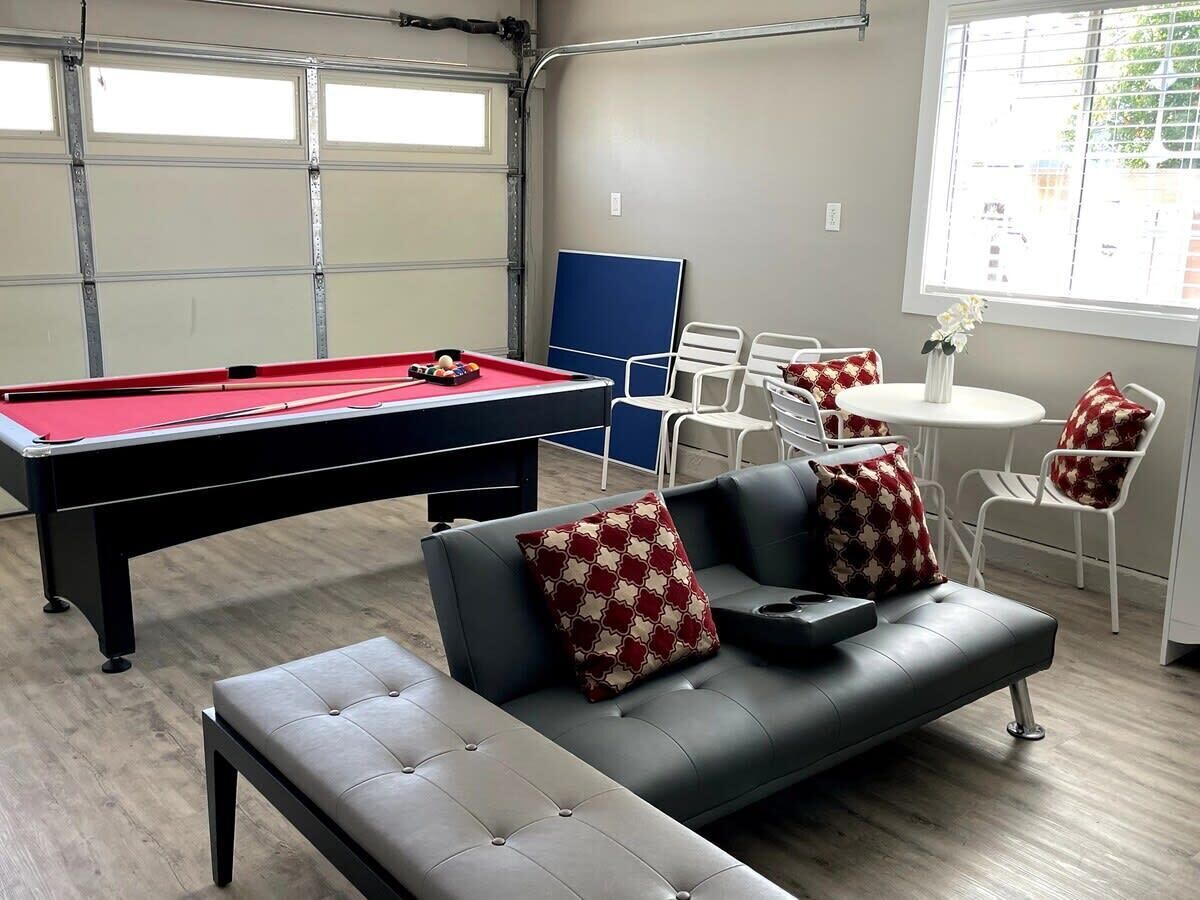 Een pooltafel in een kamer met een bank en stoelen, een blauwe deur en een raam met uitzicht.