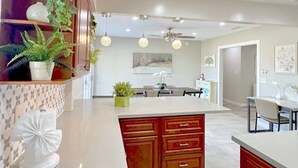 Una cocina moderna con una isla central, iluminación colgante y un comedor con mesa y sillas.