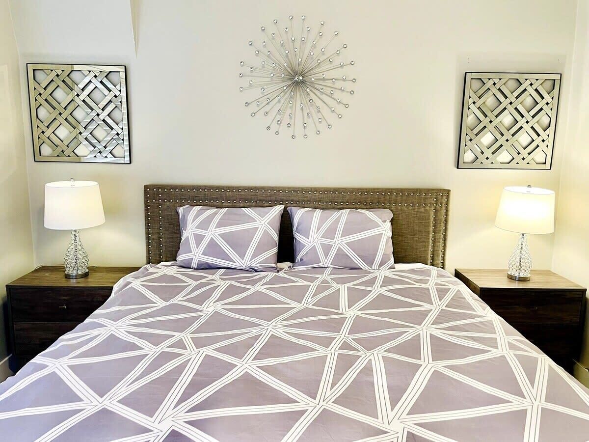 A bed with a geometric patterned bedspread, two matching pillows, a wooden headboard, and two nightstands with lamps.