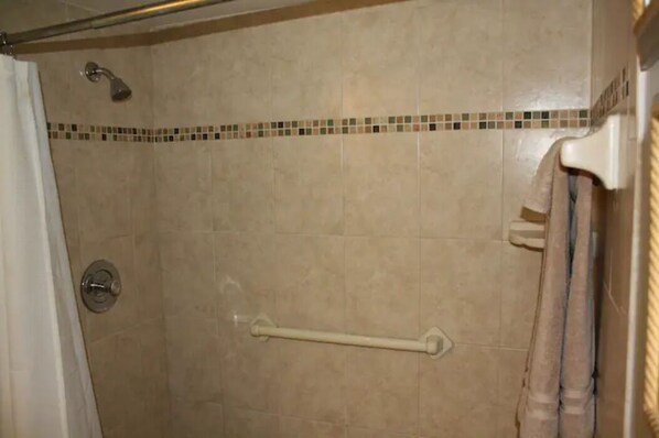 A shower area with beige tiles, a grab bar, and a showerhead. - Ocean Front Condo (Cocoa Beach)