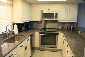 A modern kitchen with white cabinets, a stainless steel microwave, and an oven. - Ocean Front Condo (Cocoa Beach)