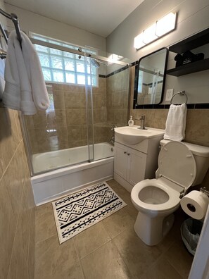 A modern bathroom with a glass-enclosed shower, a white bathtub, a sink, and a toilet.
