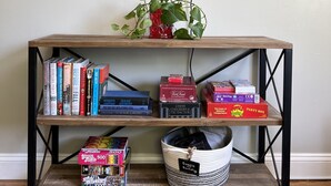 A wooden TV stand with shelves holding books, board games, and a basket. - 3 BR renovated home, near downtown Raleigh, privacy fenced backyard! (Raleigh)