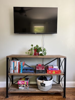 A wooden TV stand with shelves holding books, board games, and a basket.