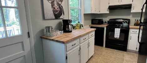 Una cocina con armarios blancos, una estufa negra y una ventana con vistas a zonas verdes.