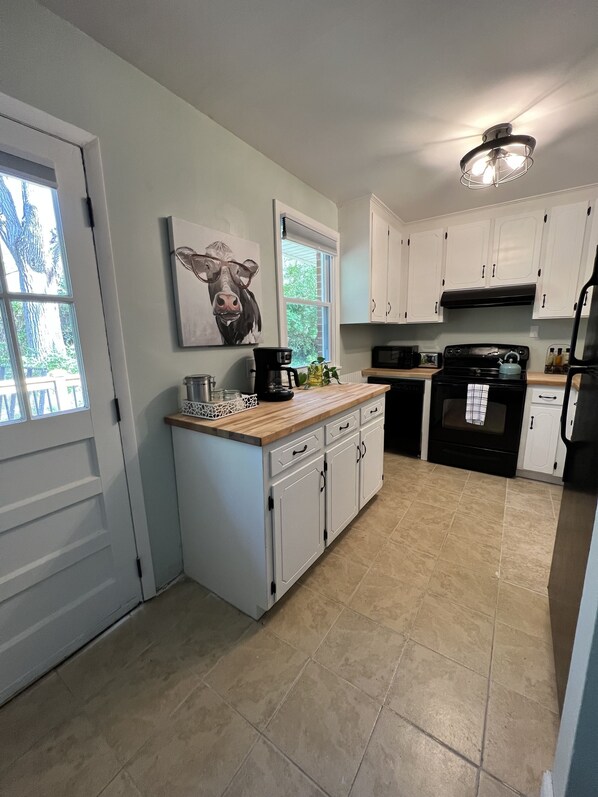 A kitchen with white cabinets, a black stove, and a window with a view of greenery.