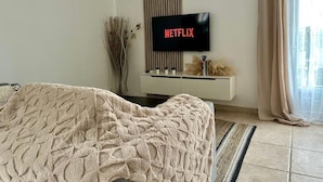 Un salon avec un téléviseur affichant le logo « NETFLIX », un canapé, un vase décoratif et une fenêtre avec des rideaux.