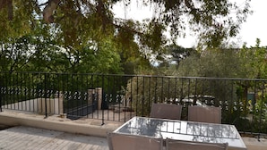 Une terrasse extérieure avec une table et des chaises en verre, entourée d’une clôture en métal et d’arbres.