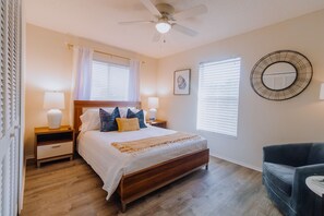 Relax in this serene bedroom with a comfortable bed, bedside tables, and a ceiling fan. Enjoy the view from the large window with blinds and a wall-mounted artwork.