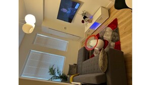 Una sala de estar moderna con un sofá gris, un televisor de pantalla plana montado en la pared, un ventilador de techo y un ventanal con persianas.