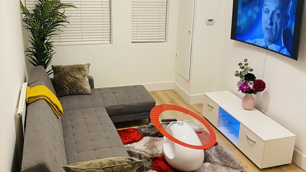 Una sala de estar moderna con un sofá seccional gris, un tapete rojo y gris, una mesa de centro blanca y un televisor de pantalla plana montado en la pared.