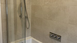 Un baño moderno con ducha envuelta en vidrio, una bañera blanca y un grifo instalado en la pared.