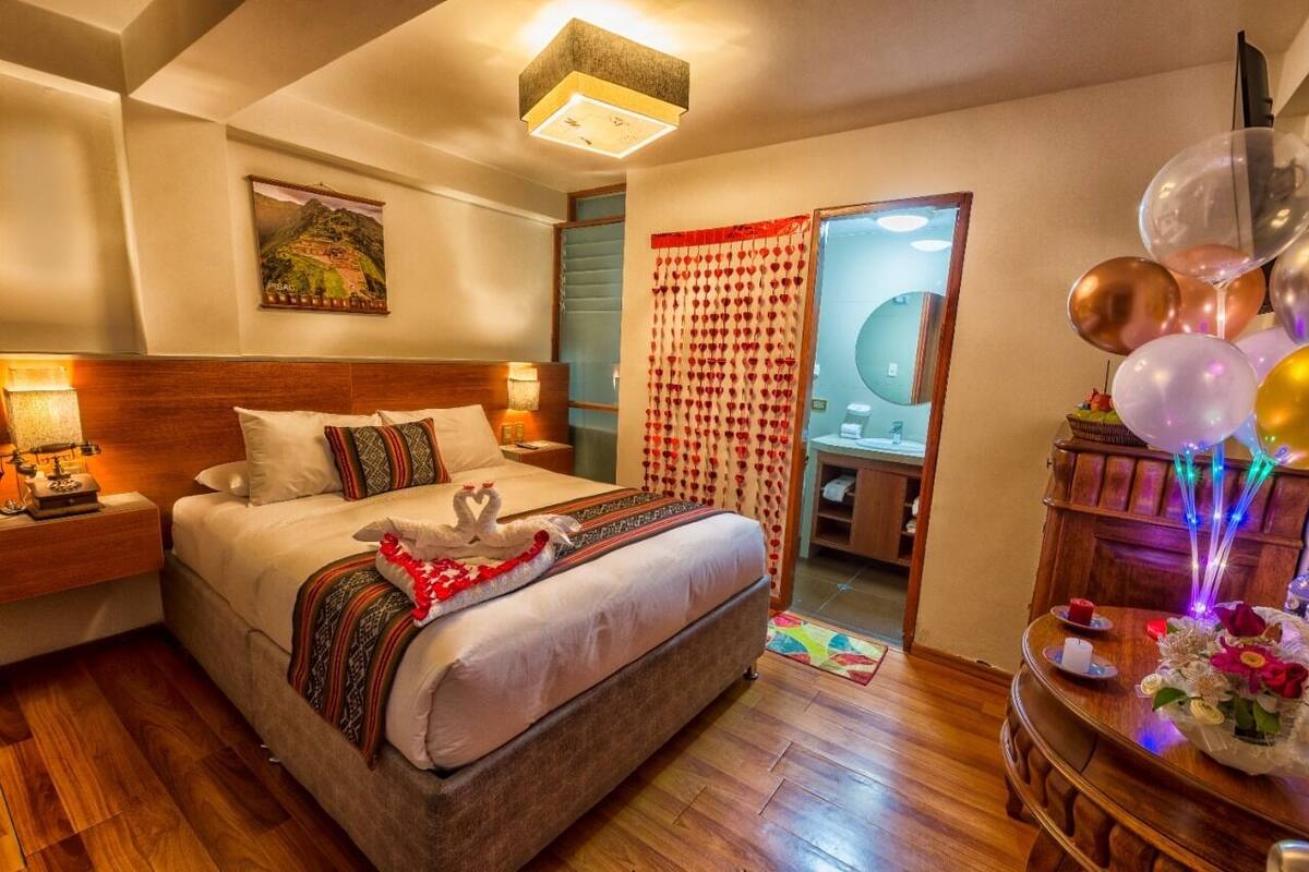 Une chambre d’hôtel avec un grand lit, une tête de lit en bois, des lampes de chevet, une table de chevet, une commode en bois et un miroir.