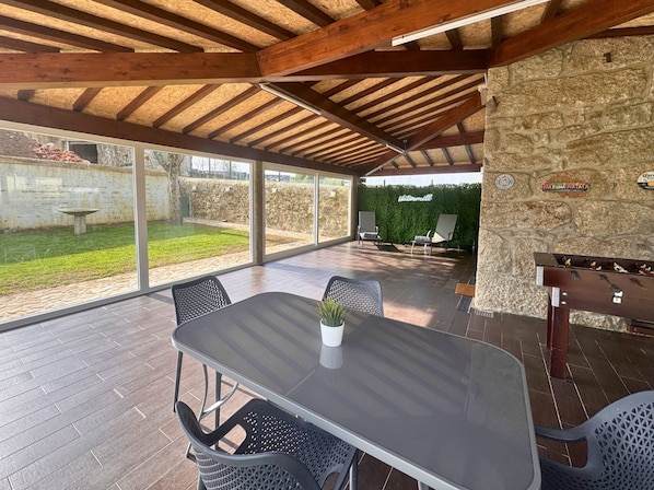 An outdoor patio with a table and chairs, a stone wall, and a view of a garden.