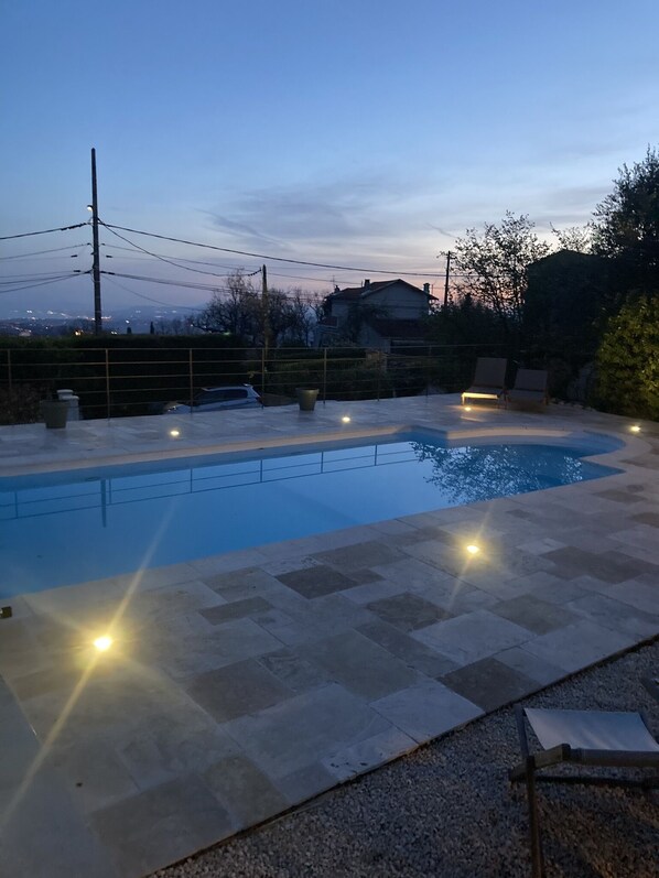 A swimming pool with a tiled deck, surrounded by a low fence, and a few lounge chairs.