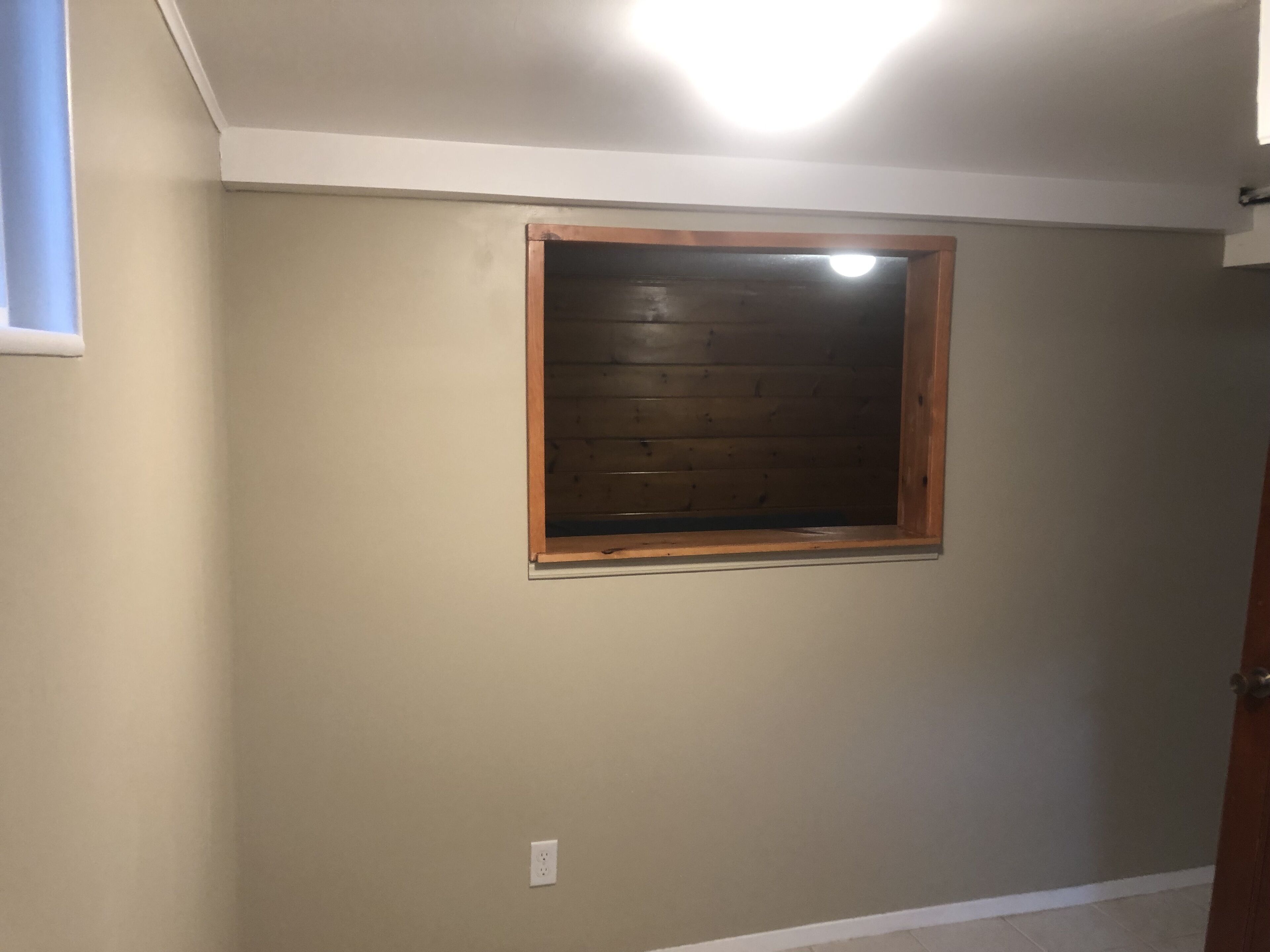 A room with a single window, a light fixture on the ceiling, and a door.