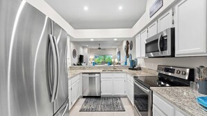 Eine moderne Küche mit Edelstahlgeräten, weißen Schränken und einer Arbeitsplatte aus Granit, mit Blick ins Freie.