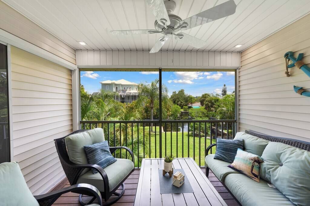 Un balcon abrité, doté d’un ventilateur de plafond, de deux canapés, d’une table et offrant une vue sur une maison et la verdure.