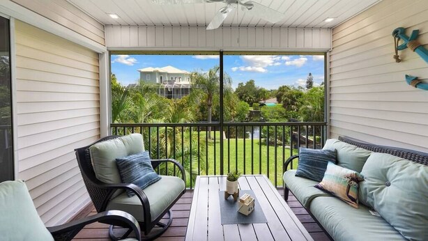 Ein überdachter Balkon mit Deckenventilator, zwei Sofas, einem Tisch und Blick auf ein Haus und Grünflächen.